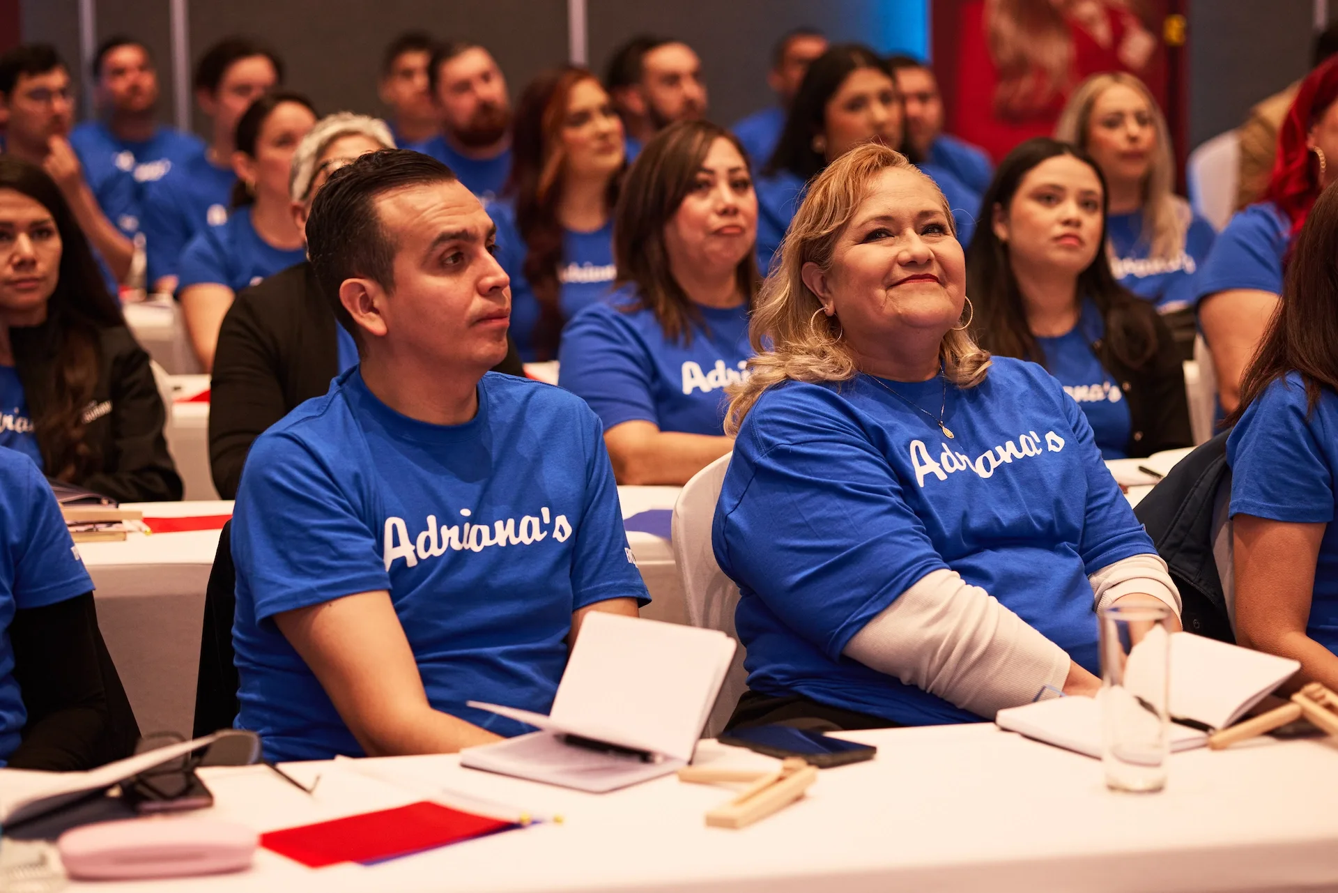 A room full of people in blue Adriana's T-shirts at a company event