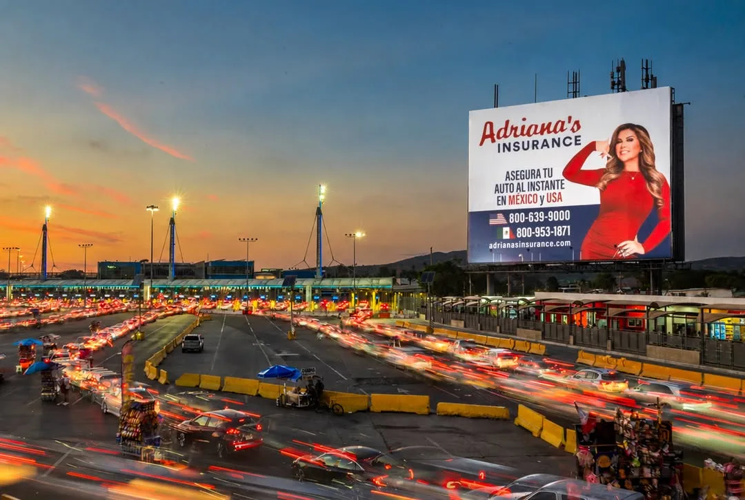 An Adriana's Insurance billboard, "Asegura tu auto al instante en México y USA", above lanes of traffic at sunset
