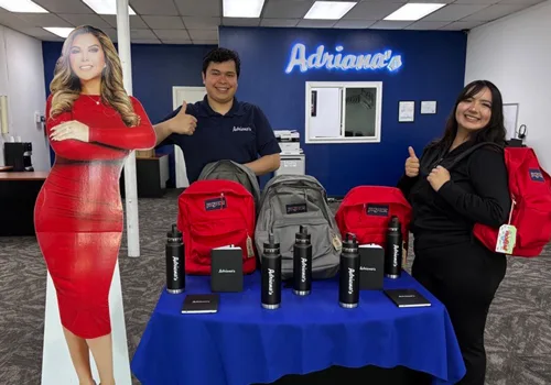 Team members beside the Adriana's sign and a table of branded backpacks